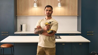 Rickie in Greenwich Matt Marine Blue kitchen, holding a yellow power drill