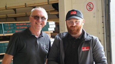 A smiling builder on the left and depot staff standing on the in a depot warehouse.